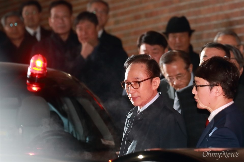 22日晚，李明博被押送至拘留所前，从家中走出