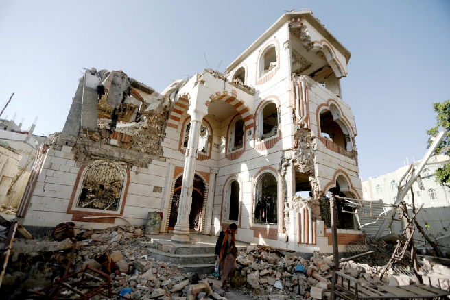 2018年3月21日，也门首都萨那，一名警卫走在被空袭毁坏的房屋的院子里。