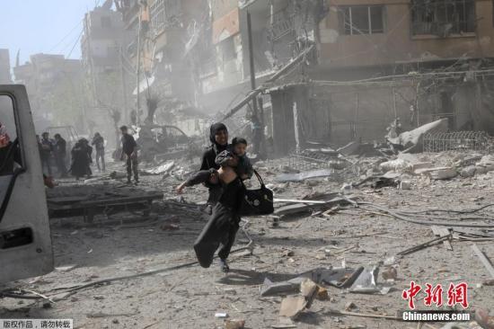 当地时间2018年3月20日，叙利亚东古塔地区当地再遭政府军空袭，一名妇女抱着孩子在废墟上狂奔。