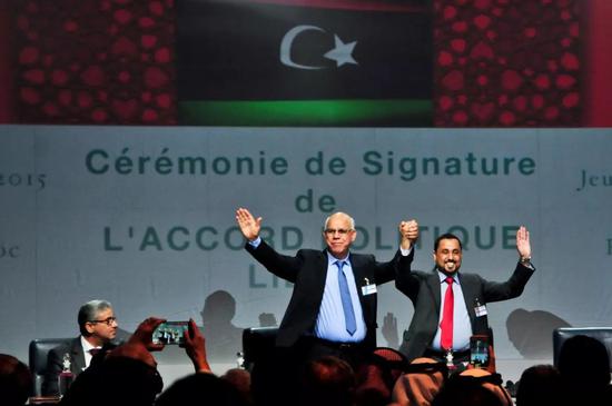 2015年12月17日，在摩洛哥斯希拉特，利比亚两个对立议会的代表在利比亚最终和平协议签署仪式上举手致意。（新华社记者 张远 摄）