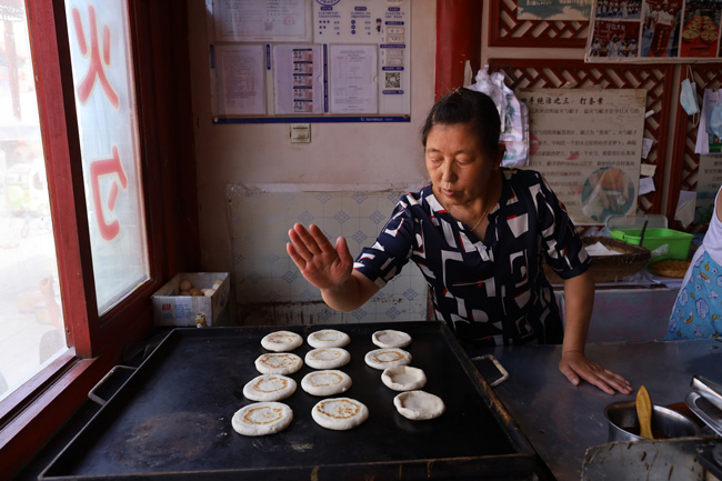 李冬梅的丈夫老陈在条案上揪着面团,再用特制的火勺槌擀成圆饼,又揪下