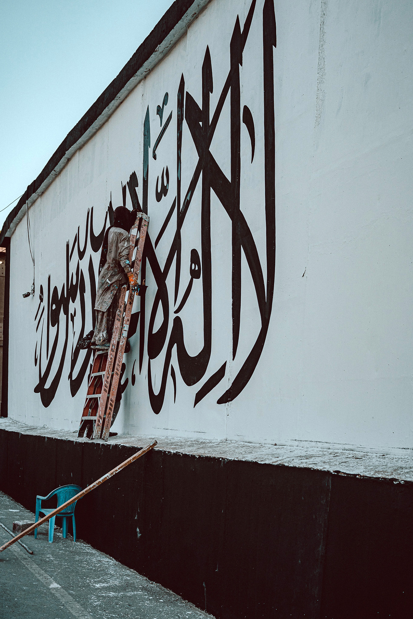塔利班在美国大使馆墙上画巨幅旗帜：踩梯子绘制 路人围观